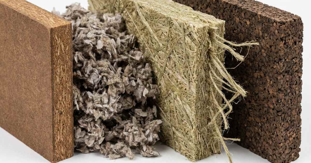 Quatre échantillons d'isolants écologiques côte à côte montrant un panneau de fibre de bois brun à gauche, un tas de flocons de ouate de cellulose, un panneau de chanvre beige-vert à fibres longues et une plaque de liège expansé granuleux à droite